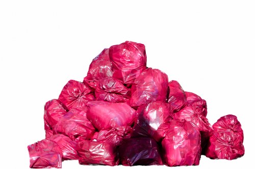 A collection of multiple pink plastic rubbish bags, tightly sealed and piled in a random formation, occupying the foreground of the image. The bags appear to be made of shiny, flexible plastic material and are filled with waste, causing them to bulge and create irregular surface textures. The pile is situated on an unspecified surface with a plain, light-colored background, and the bags vary slightly in size but are generally similar in shape. This scene illustrates typical waste collection or removal of household rubbish, which could be relevant to services offered by Rotherhithe House Clearance. The image emphasizes waste management practices within a UK context, especially pertaining to local rubbish disposal needs in a residential or urban environment.