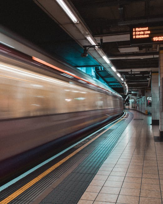 A London Underground station platform with beige tiled walls and wooden ceiling panels. Advertisements and station signage are visible along the wall, including a red and white sign for the 'Blackfria